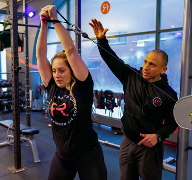 Personal trainer coaching a woman during a cable exercise in a semi-private training session