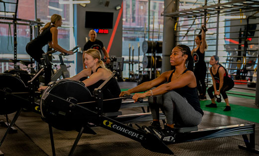 Members using rowing machines during a coached group fitness class at a boutique training studio